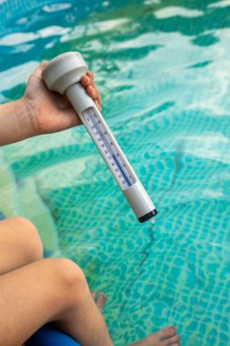 Yüzme havuzundaki suyun sıcaklığını ölçen bir kadının dikey görüntüsü.