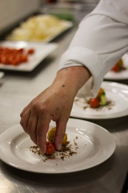 Profesyonel bir aşçının, restoranın mutfağındaki yemeğe son tasarımlarını eklediği dikey yakın plan bir fotoğraf.