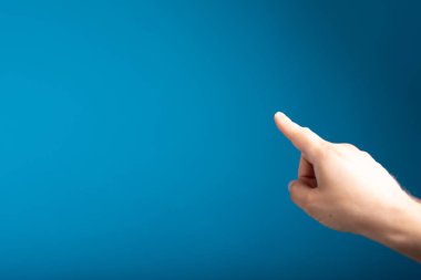 Mavi arka planda bir yeri işaret eden bir parmağın yakın plan çekimi.