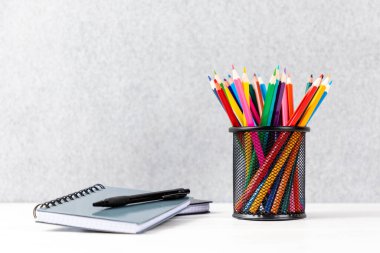 Masasında gri bir not defteri olan siyah sepetteki renkli kalemler.