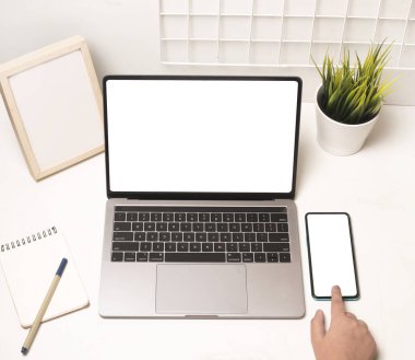 Dizüstü bilgisayar ve cep telefonu kullanan ve ofiste boş ekranı olan bir kadın elinin üst görüntüsü.