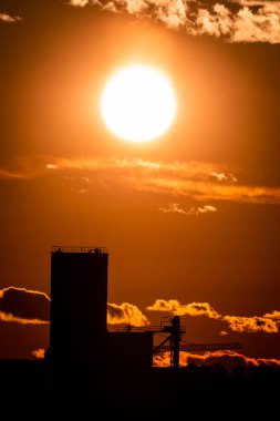 Modern bina siluetleri üzerinde parlayan turuncu bir günbatımı gökyüzünün dikey görüntüsü