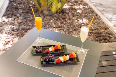 Tahta çubuklarda taze meyveler ve masada kokteyller..