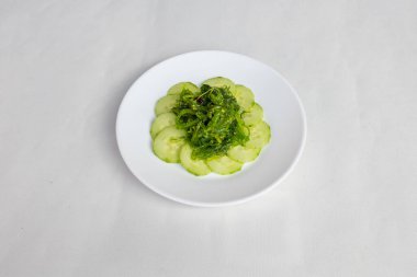 Beyaz bir tabakta dilimlenmiş salatalıklı yeşil yosun salatası.