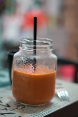 Tayland restoranındaki ahşap bir masada pipetle bir Tayland sütlü çayının dikey yakın çekimi.