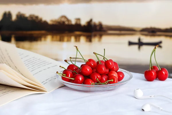 Ένα Πιάτο Κόκκινα Ώριμα Κεράσια Στο Τραπέζι Ένα Βιβλίο Και — Φωτογραφία Αρχείου