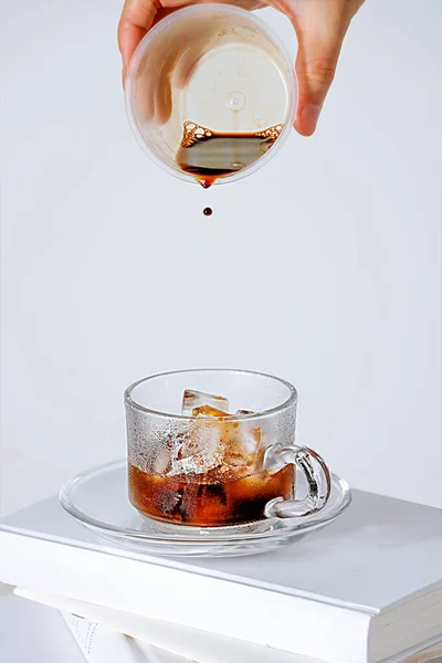 白い背景に氷のキューブとカップにコーヒーを徐々に追加する手の垂直ショット — ストック写真