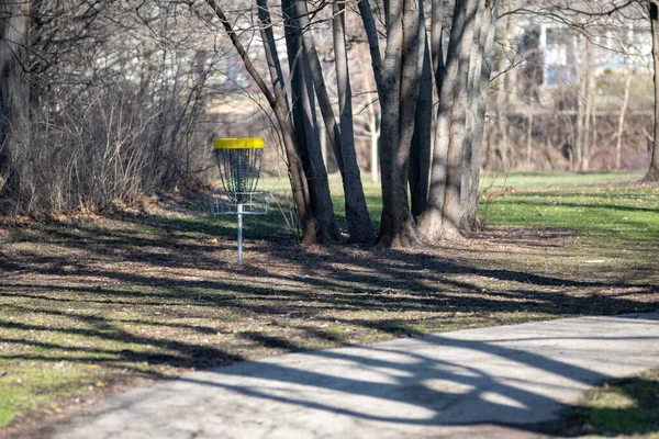 A disc golf target under the shadow of the trees in the park