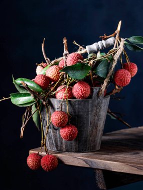 Tahta bir masada metal bir sepetin içinde yeşil yapraklı taze olgun liçi meyvesi manzarası.