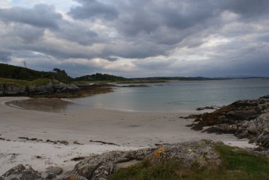 İskoçya 'da bulutlu bir gökyüzünün altında kayalık kıyı ve dağ manzarası