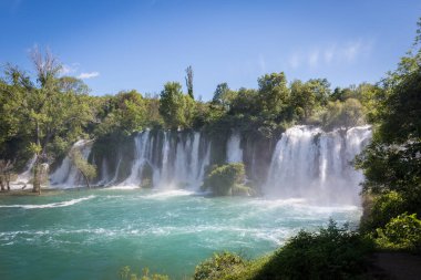 Parlak güneş ışığının altında akan bir şelalenin manzarası.