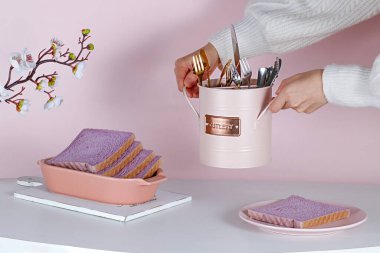 Mor tatlı ekmek, çatal bıçak seti ve çiçeklerle estetik bir masa hazırlayan biri.