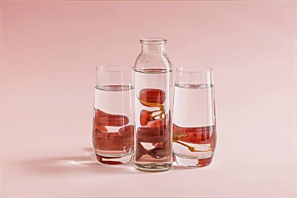 水の透明なボトルとピンクの背景にブドウの後ろに2つのグラス — ストック写真