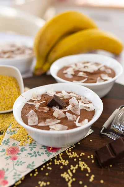 A board with two bowls of chocolate mousses and banana near the board