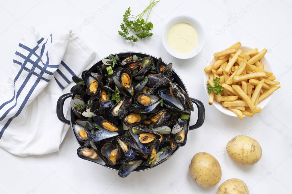 A top view shot of Belgian mussels with potato fries and sauce on a white marble table