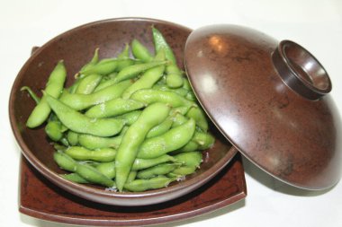 Kahverengi bir kâsede kaynamış bir edamame tabağı.