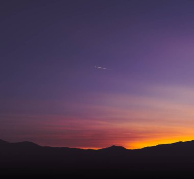 Kayan bir yıldız ve dağların siluetiyle güzel bir gün batımı.