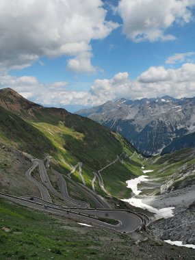 Güneşli bir günde mavi bulutlu bir gökyüzünün altında tepelerde ve dağlarda motosikletli bir yol.