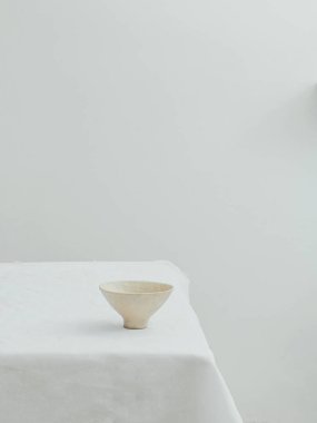 Masanın üzerinde beyaz masa örtüsü olan minimalist bir kâsenin estetik görüntüsü.