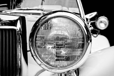 Fotoğraf siyah beyaz ve üstü açık bir arabanın kısmi ön görüntüsünü gösteriyor. Bir sürü krom aracı süslüyor.