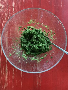 Kırmızı ahşap arka planda ince doğranmış bitkilerle dolu cam bir kâsenin dikey görüntüsü.