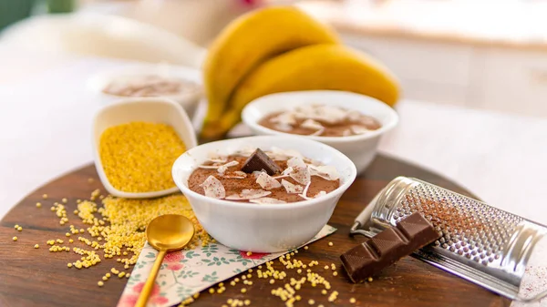 A board with two bowls of chocolate mousses and banana near the board