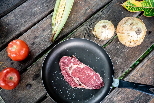 トウモロコシ トマト 玉ねぎのある木のテーブルの上に 味付け生ステーキ付きの黒パンの上からの眺め — ストック写真
