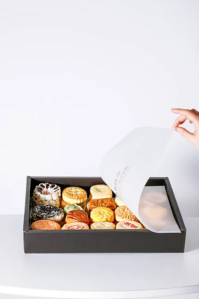 A vertical shot of a person opening a box of different types of desserts on a white background