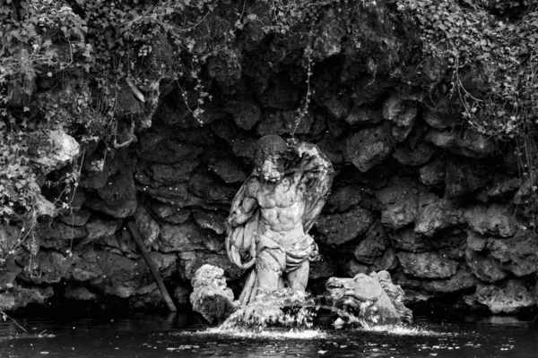 A grayscale shot of a sculpture in the water in the background of a rocky cave.