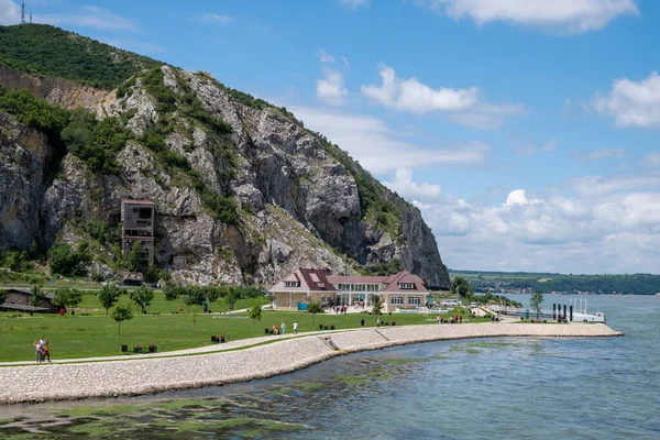 A scenic waterfront landscape with a building, people, a lawn, and cliffs