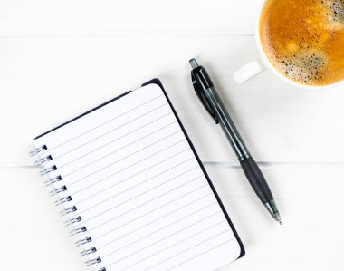 Beyaz ahşap arka planda kağıt ve kalemle yakın plan kahve fincanı.