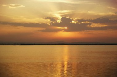 Turuncu akşam gökyüzünün manzarası bir su kütlesine yansıyor.