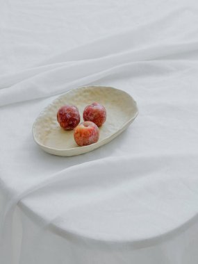 Beyaz kumaş kapaklı bir masada beyaz bir kasede elmaların dikey estetik görüntüsü.