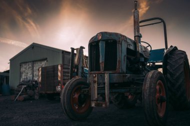 Bir çiftlikte logosu olan paslı eski bir traktörün resmi. Parlayan gökyüzünün altında.