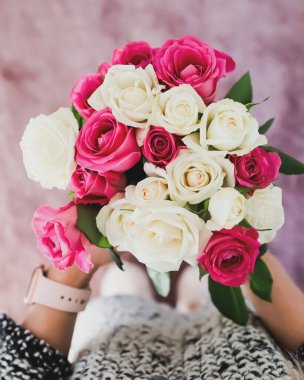 Parlak pembe ve beyaz bir gül buketi tutan bir kadının dikey odak noktası.