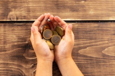 Kahverengi ahşap arka planda bozuk paralarla dolu yetişkin ellerinin üst görüntüsü