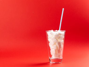 Bir bardak şeker küpü ve kırmızı arka planda bir pipet.