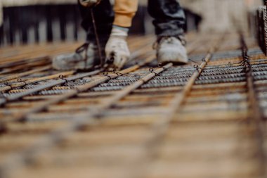 Paslı beton takviyeli çelik parmaklıklar üzerinde çalışan bir işçinin seçici odak noktası.