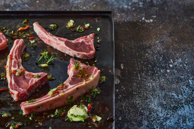 Pişmemiş kuzu pirzolası, doğranmış sebzeler ve siyah tavada yağ.