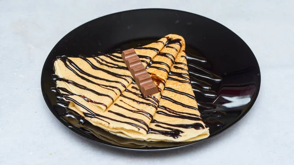 A closeup shot of crepes with chocolate syrup and candy on a black plate