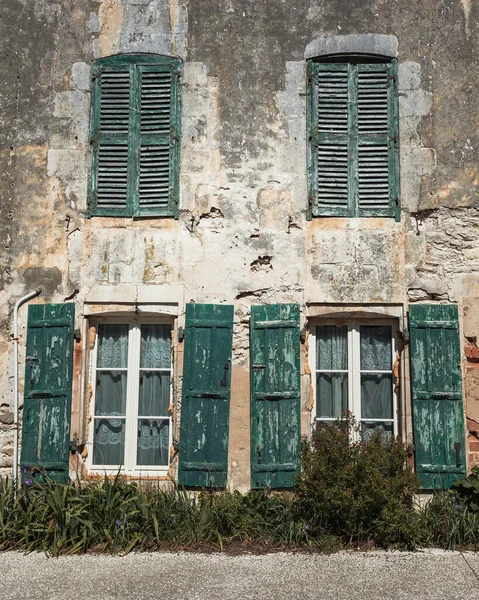 A facade of a destroyed house with windows with green shutters