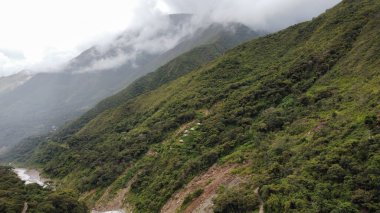 Dağların arasından akan bir nehrin manzarası bulutlu bir gökyüzünün altında yeşilliklerle kaplı.