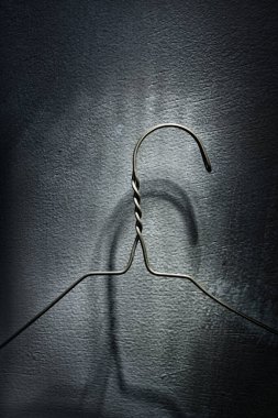 Beton bir duvara uğursuz bir gölge düşüren eski metal tel bir elbise askısının dikey çekimi.