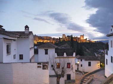 İspanya 'da alacakaranlıkta ön planda beyaz geleneksel binalar bulunan bir Alhambra.