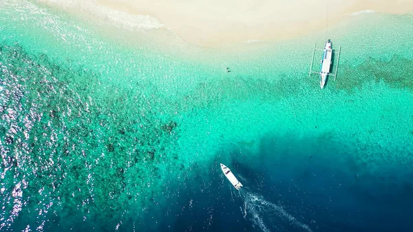 An aerial top view of yachts floating in turquoise water by a beach in the Maldives