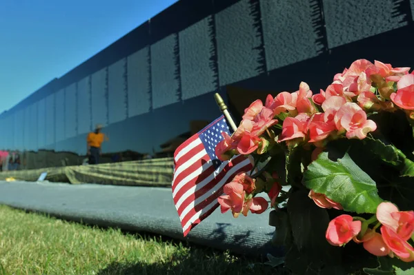 A closeup of pink flowers and the American flag against the Vietnam Veterans Memorial Wall in Medina, Ohio
