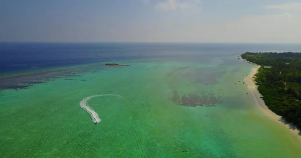 A bird's-eye view of a boat next to a tropical island in the azure ocean