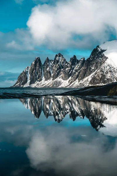 A beautiful scene of snow mountains reflecting on eater against a blue cloudy sky in Norway