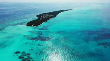 Güneşli bir günde, turkuaz bir denize karşı yeşillikle kaplı bir adanın havadan görünüşü.