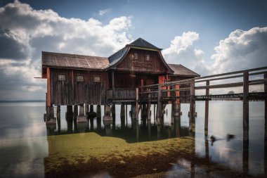 Almanya 'nın Bavyera kentindeki bulutlu gökyüzüne karşı Ammersee Gölü üzerinde güzel bir kayıkhane manzarası
